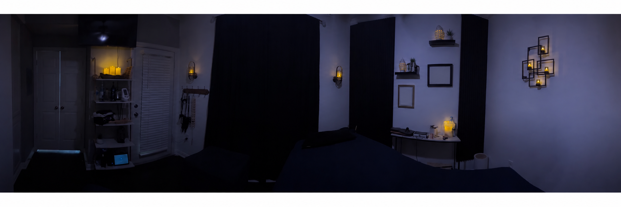 Partial panorama of Robin's massage studio with a massage table, dark curtains, shelves, and warm candle lighting.
